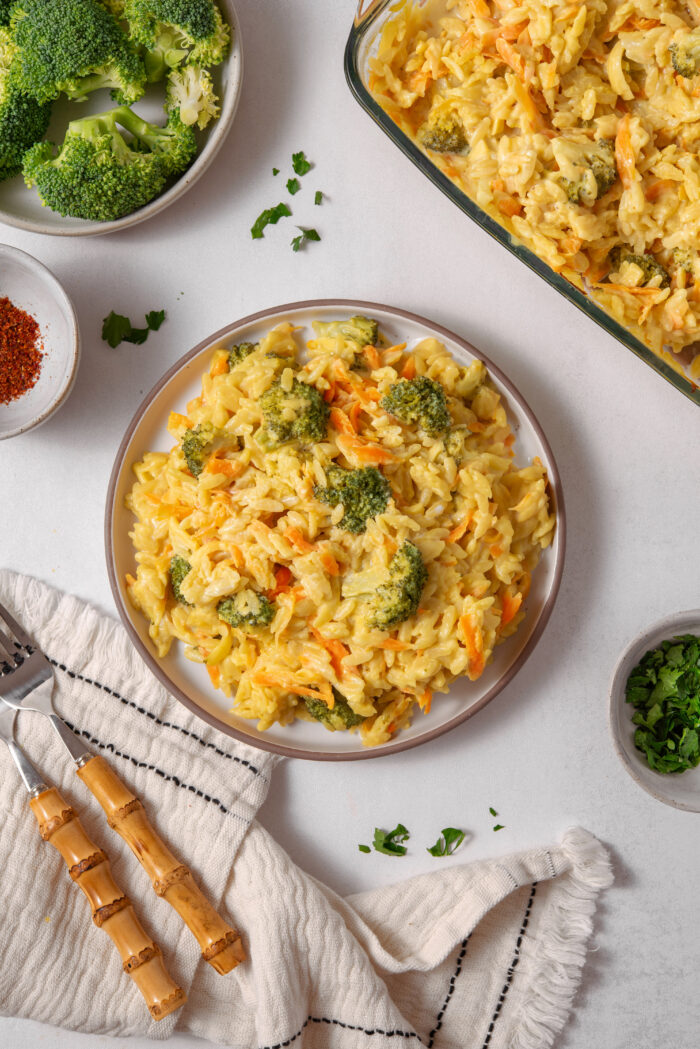 A serving of vegan broccoli cheddar orzo on a plate, with other ingredients visible in the frame.