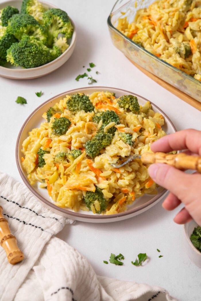A hand scooping up some vegan broccoli cheddar orzo with a fork.