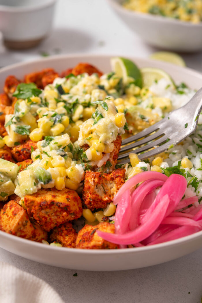 A close up of a fork digging into a serving of street corn bowls with rice and tofu.