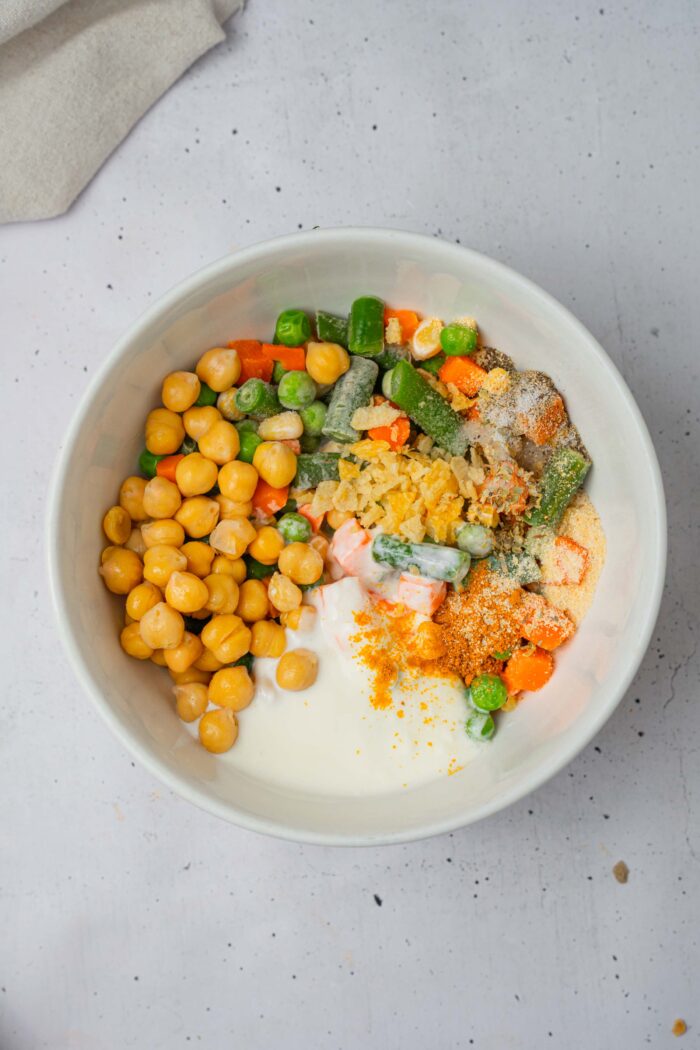 Chickpeas, frozen veggies, coconut milk and seasonings in a bowl.