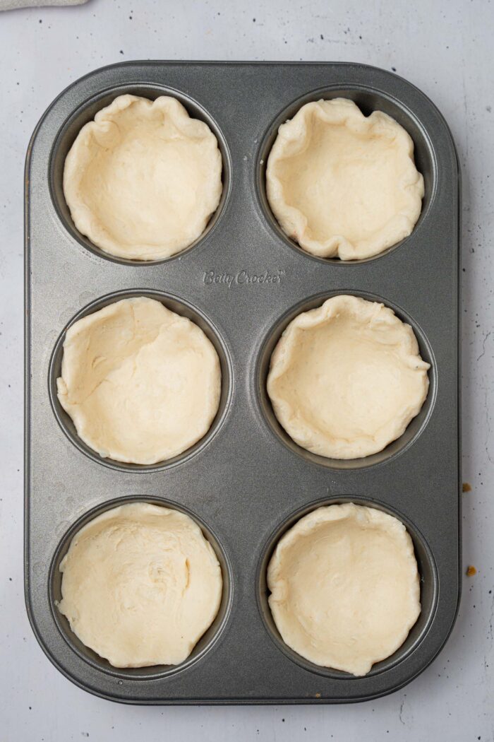 Biscuit dough spread into each "cup" of the muffin tray.
