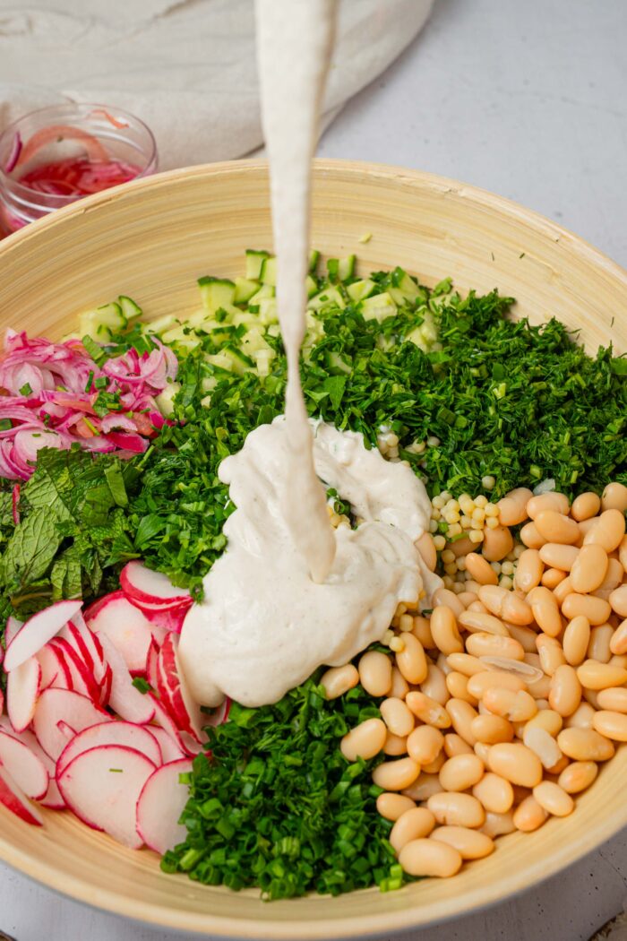 Vegan ranch dressing being added to the mixing bowl with the rest of the ingredients of the herby ranch couscous salad.