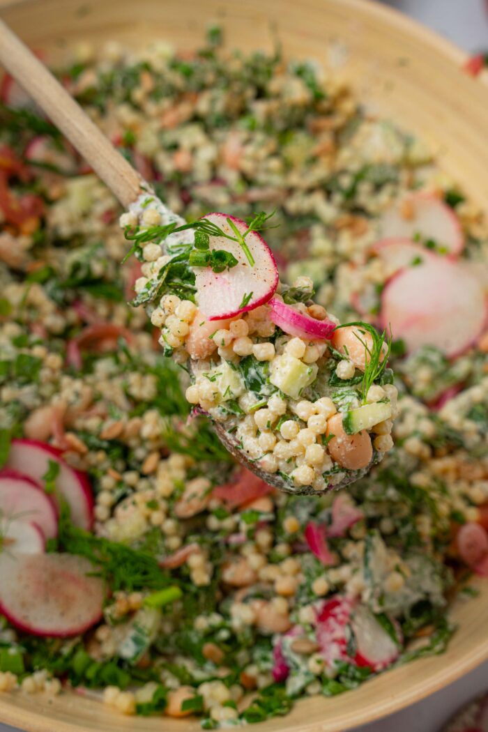 A spoonful of herby ranch couscous salad at the foreground, with the rest of the mixing bowl visible behind it.