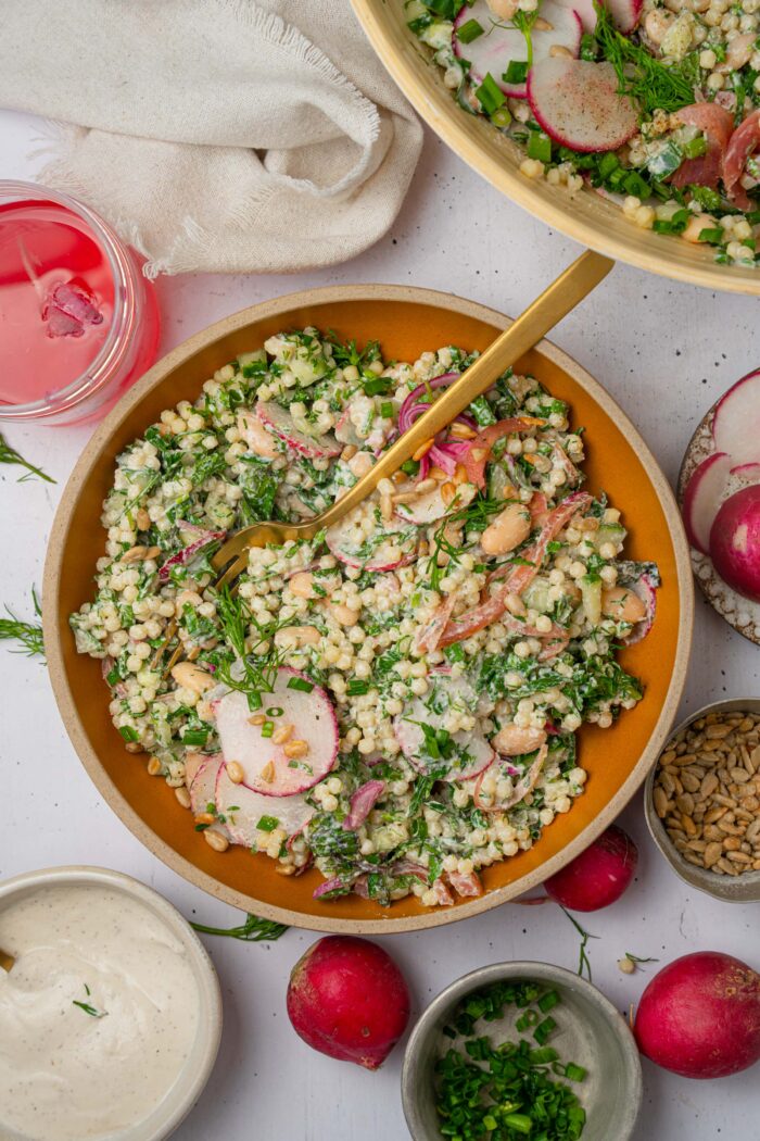 Top down view of the herby ranch couscous salad served in a bowl, with a fork sticking out of the food.