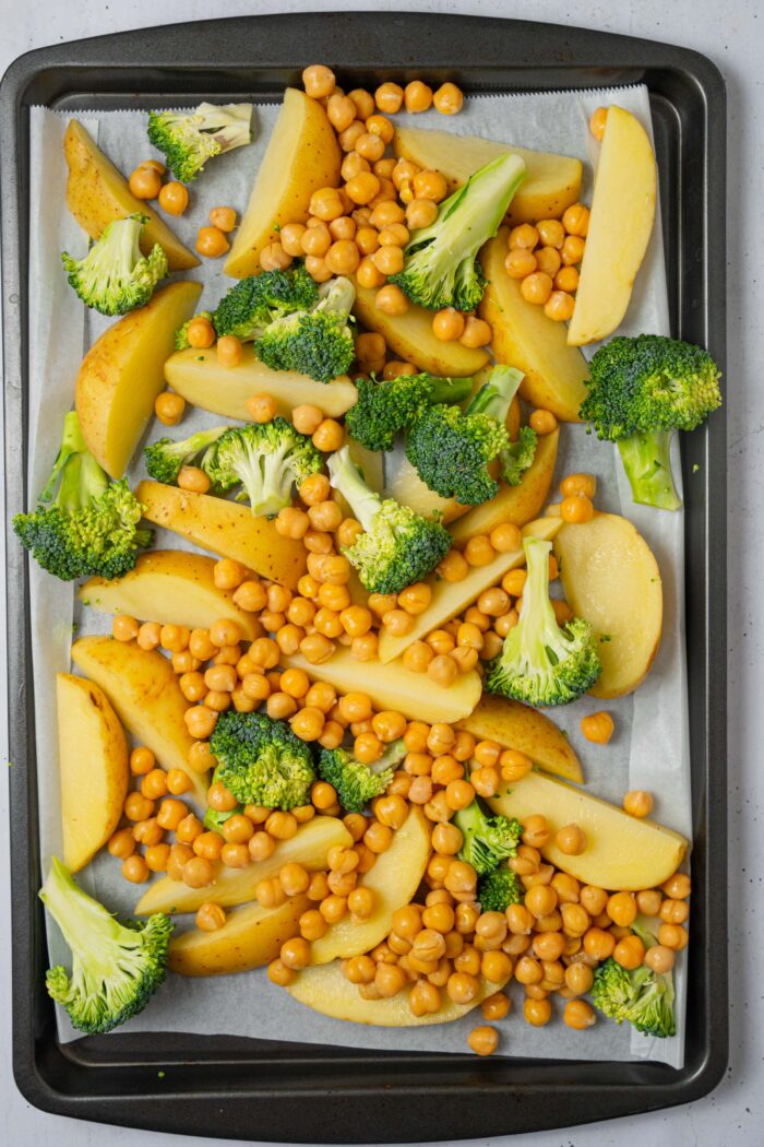 Chickpeas, potatoes and broccoli laid out on a lined sheet pan.
