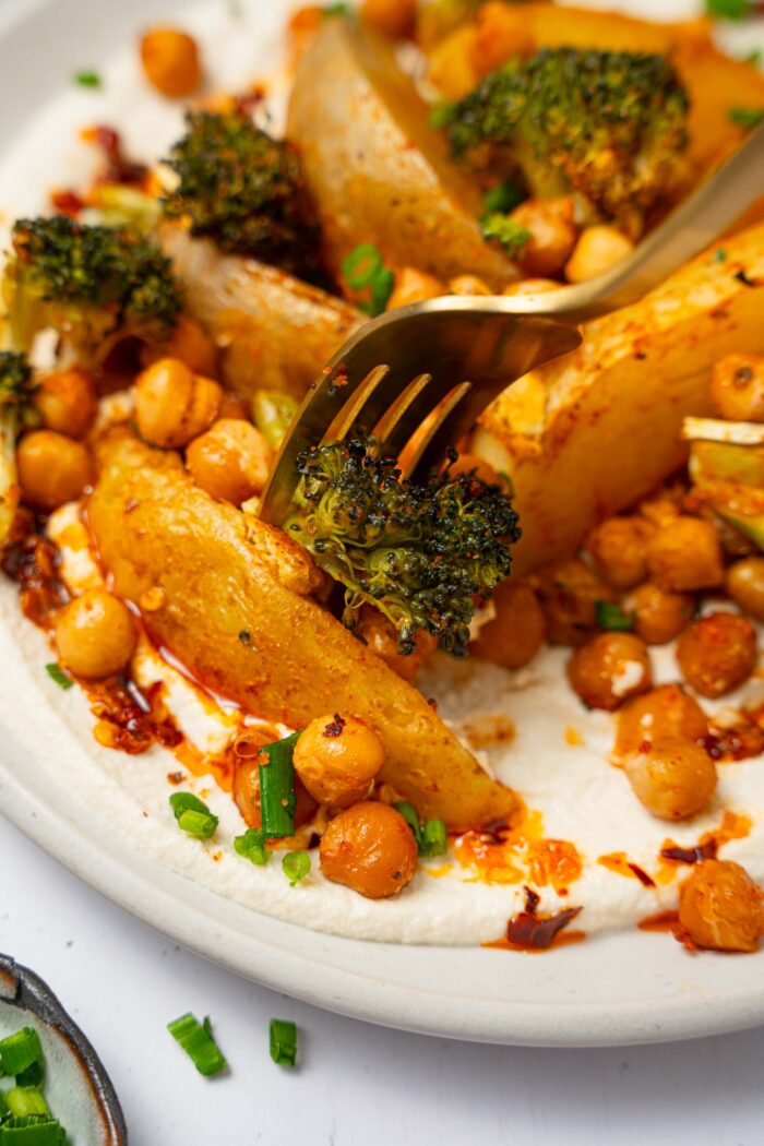A close up of a fork picking up a piece of broccoli from a plate of vegan sheet pan dinner.