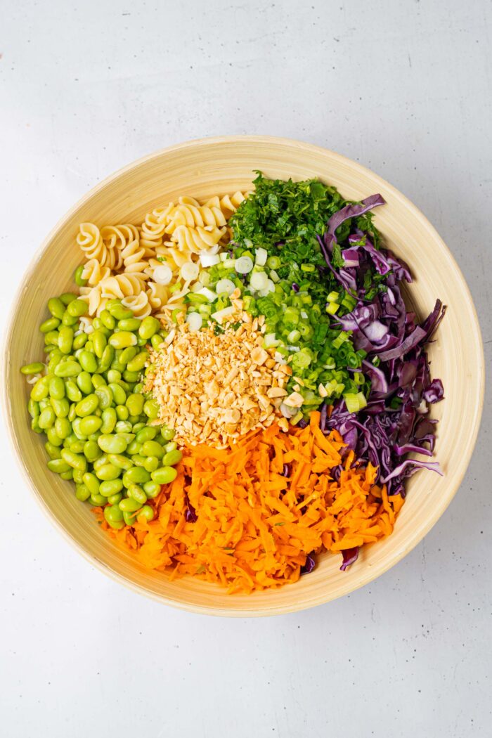 A wooden mixing bowl with all of the prepped peanut pasta salad ingredients added into it.