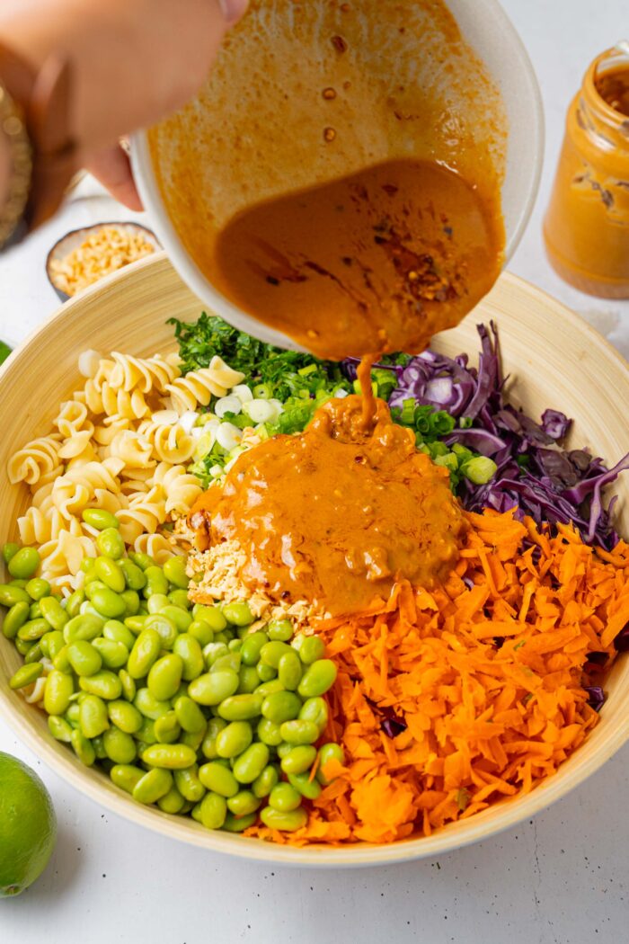 Peanut salad dressing being poured over the other ingredients in a large wooden mixing bowl.