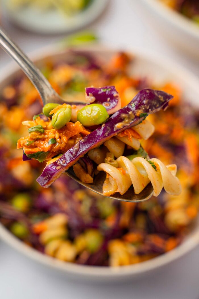 A close up of peanut pasta salad spoonful, with the rest of the serving visible in the background.
