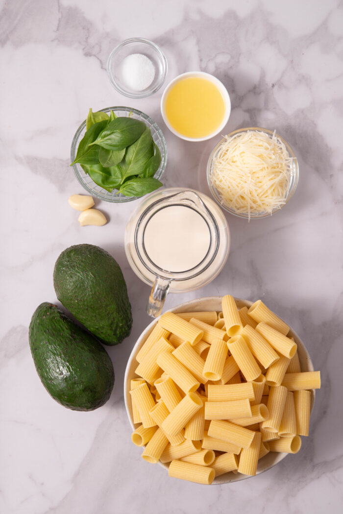 The ingredients to make quick vegan avocado pasta, laid out on a light background.
