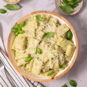Top down shot of avocado pasta served in a bowl with vegan cheese and basil.