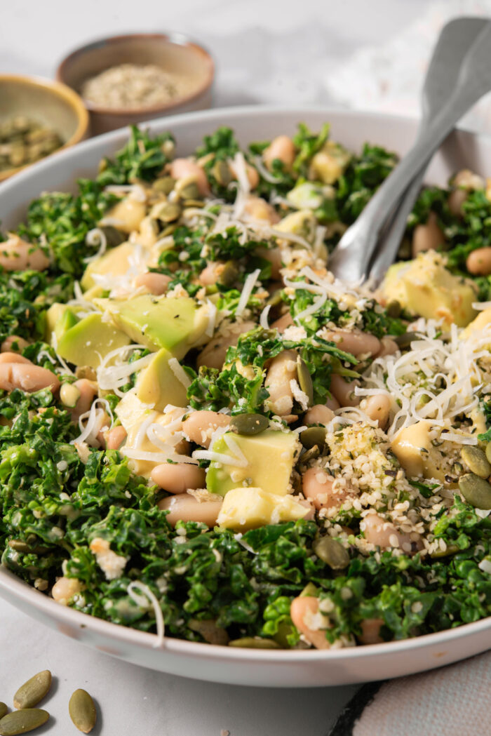 A close shot of the chopped kale salad in the mixing bowl, topped with vegan cheese.