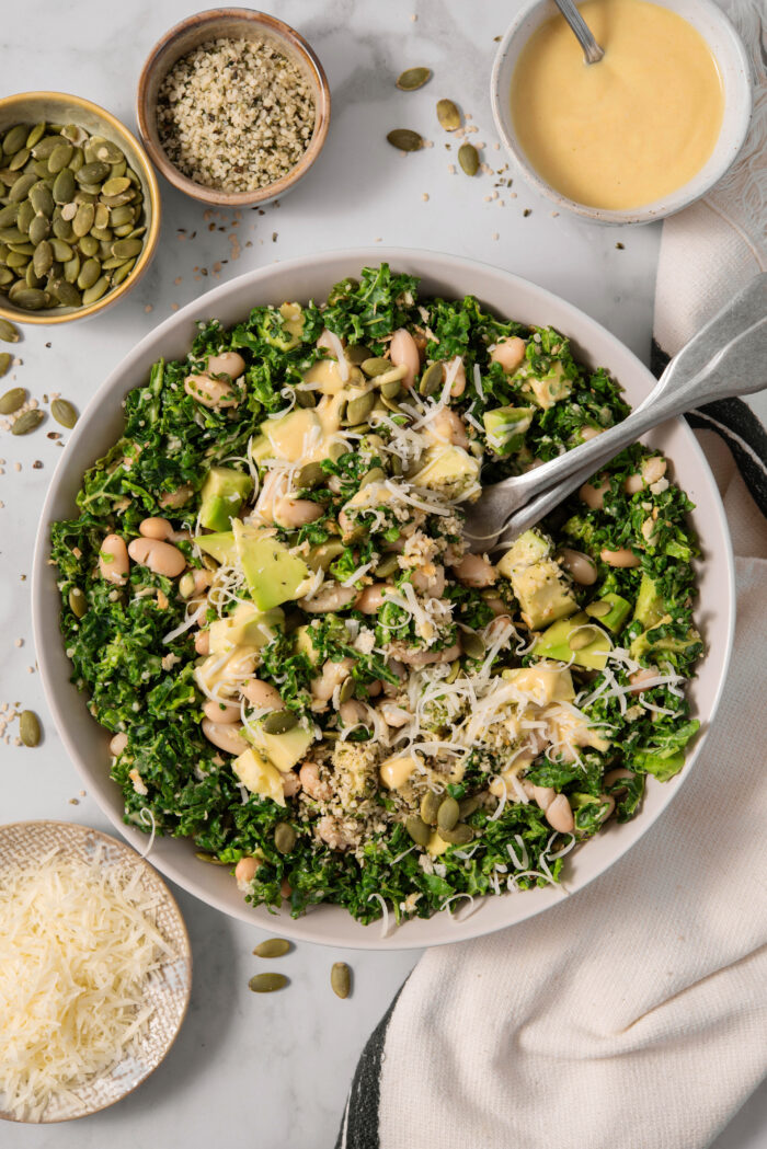 Large salad bowl of chopped kale salad with vegan parmesan, avocado, beans, and hemp hearts.