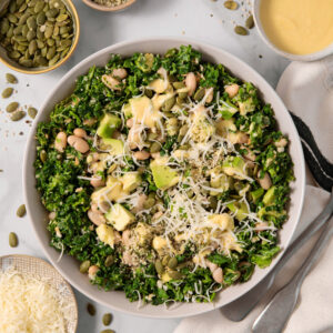Chopped kale salad, topped with vegan parmesan, and surrounded by the ingredients included in the recipe.
