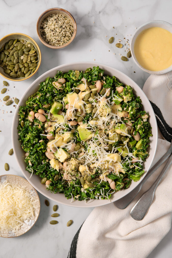 Chopped kale salad, topped with vegan parmesan, and surrounded by the ingredients included in the recipe.