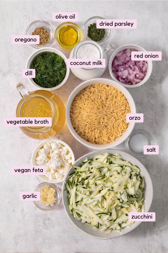 The ingredients for the creamy zucchini orzo, laid out and labeled on a clear blackground.