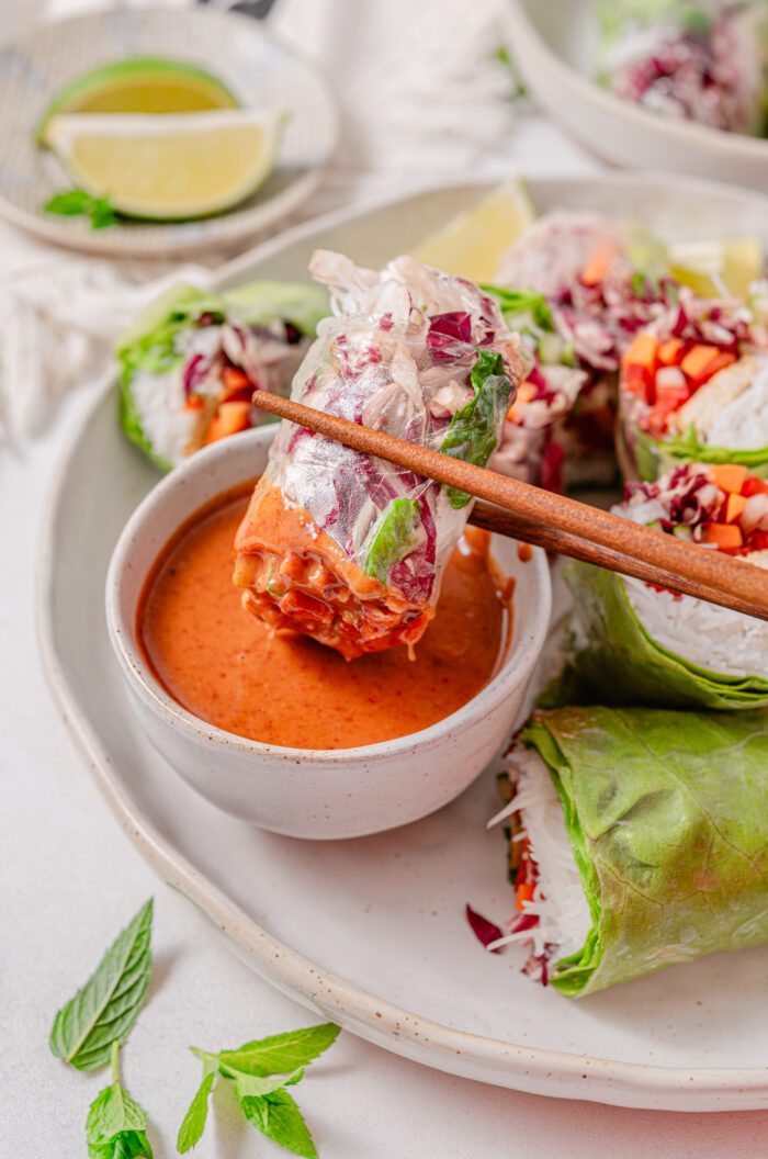 A rice paper roll being dipped into almond sauce.