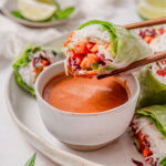 A vegan summer rolls hold up by chopsticks to the camera.
