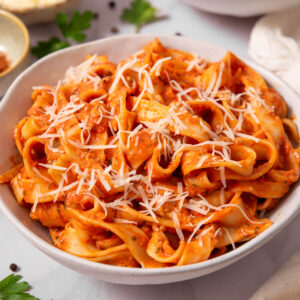 A large serving of creamy eggplant pasta in a ceramic bowl, topped with some vegan parmesan.