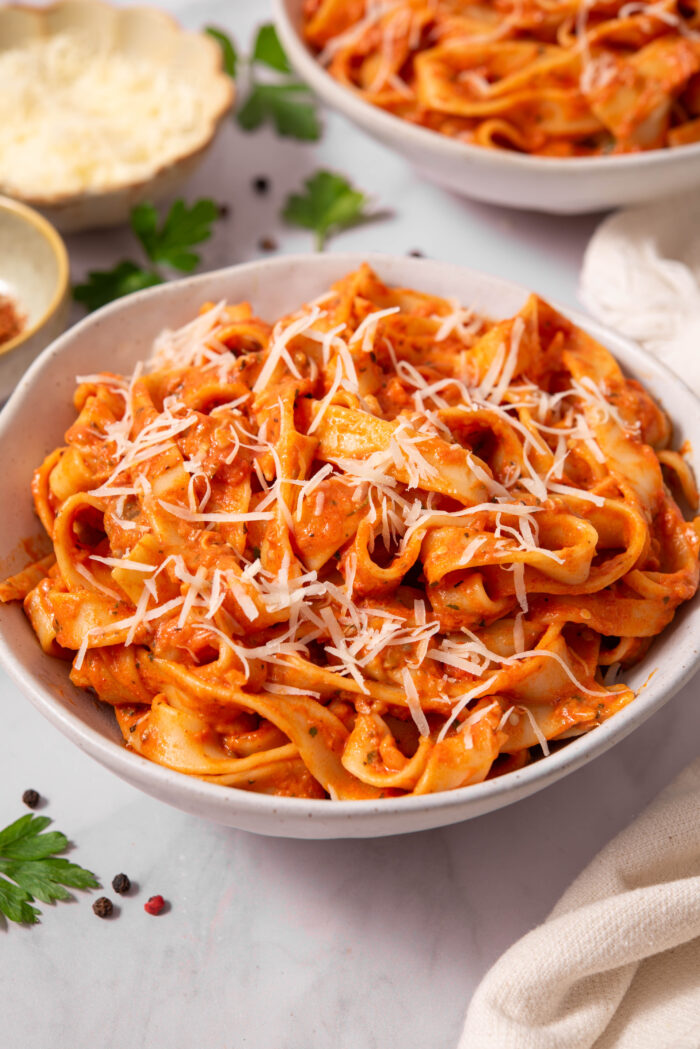 A large serving of creamy eggplant pasta in a ceramic bowl, topped with some vegan parmesan.