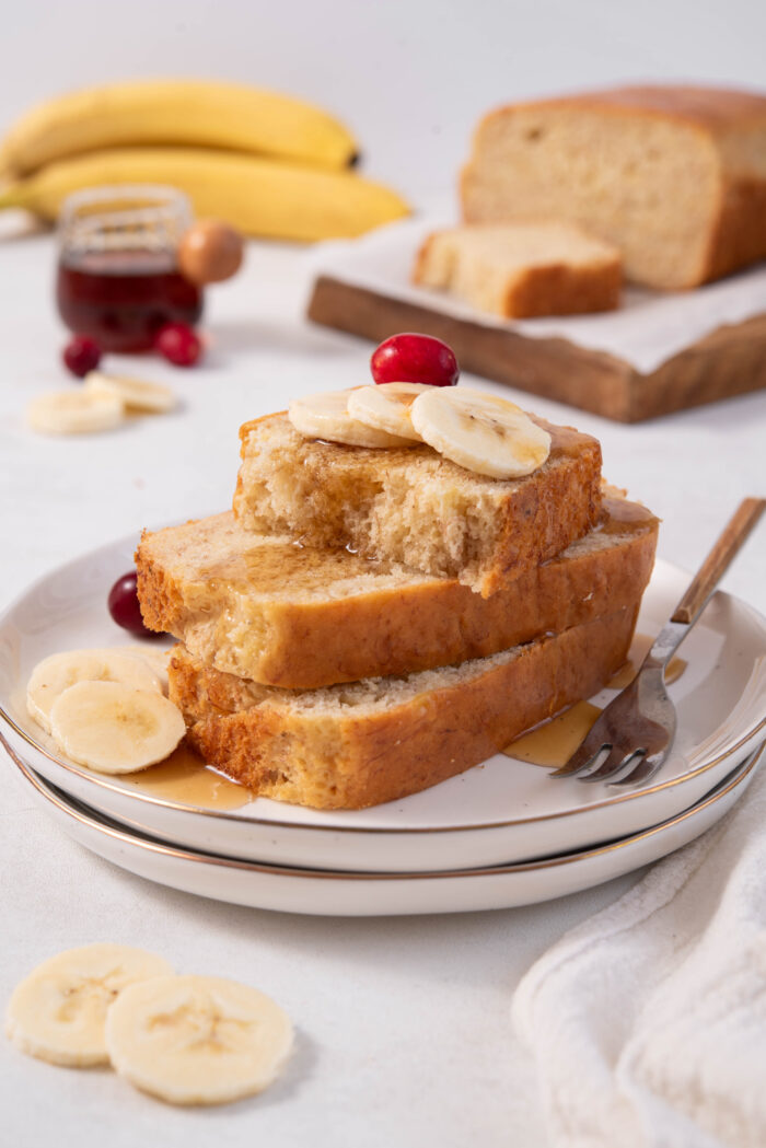 A stack of easy vegan banana bread sliced, topped with fresh banana and maple syrup.