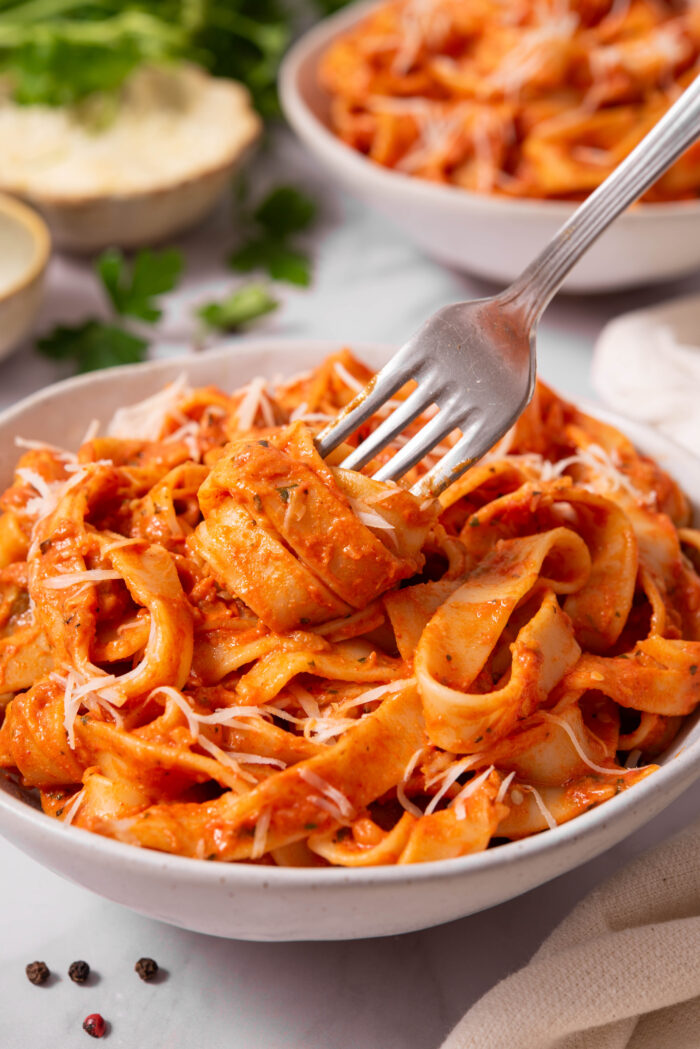 A fork digging into a bowl of creamy eggplant pasta with vegan parmesan.