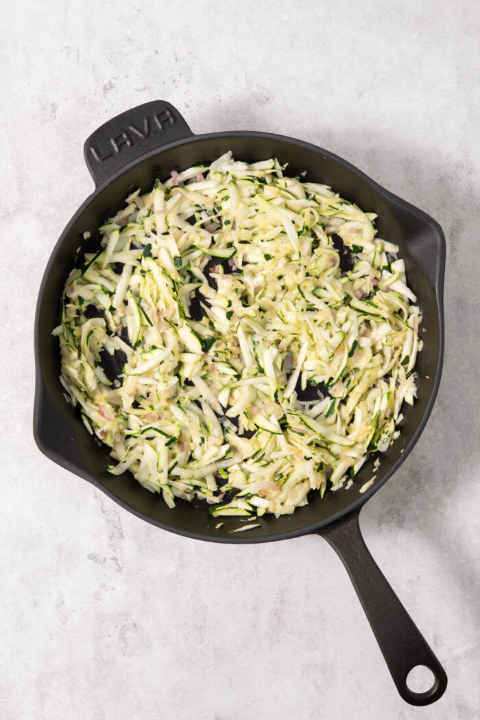 Grated zucchini in a large cast iron pan.