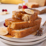 A stack of easy vegan banana bread sliced, topped with fresh banana and maple syrup.