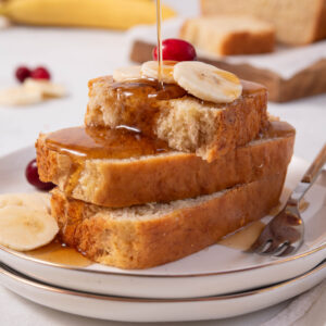 A stack of easy vegan banana bread sliced, topped with fresh banana and maple syrup.