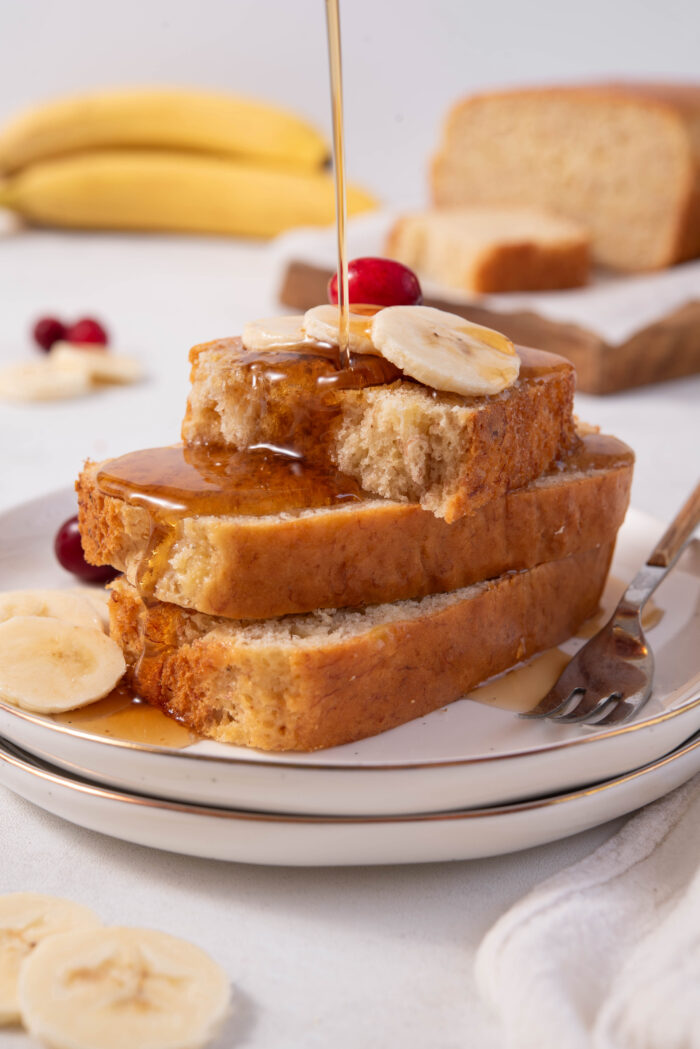 A stack of easy vegan banana bread sliced, topped with fresh banana and maple syrup.