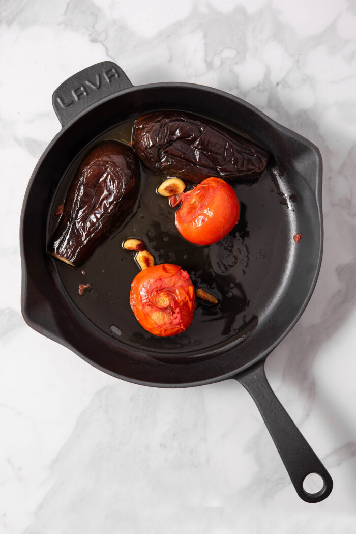 An eggplant and two tomatoes in a skillet with oil.