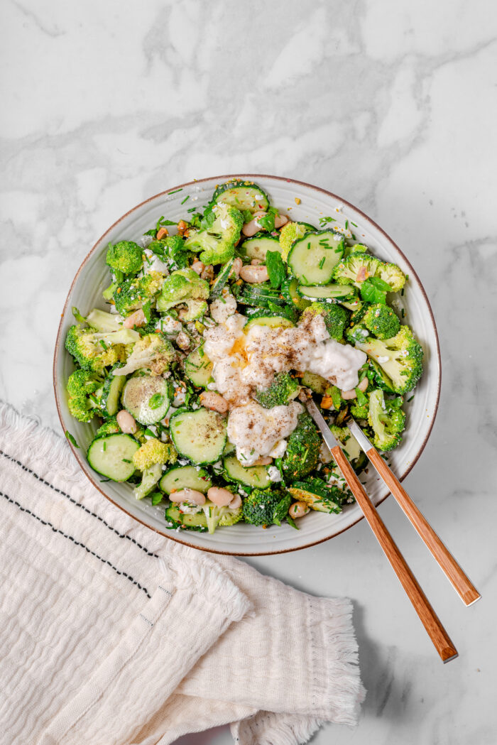 Dressing poured over the bowl of broccoli cucumber salad, ready to mix everything together.