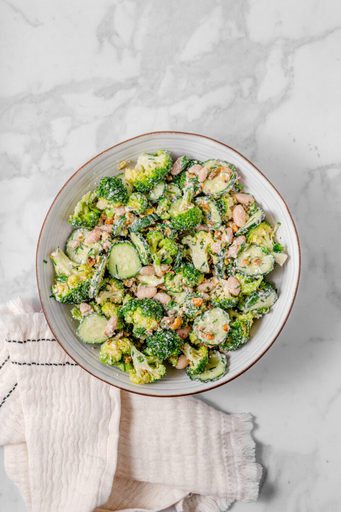 A bowl of broccoli cucumber salad mixed together with the dressing in the mixing bowl.