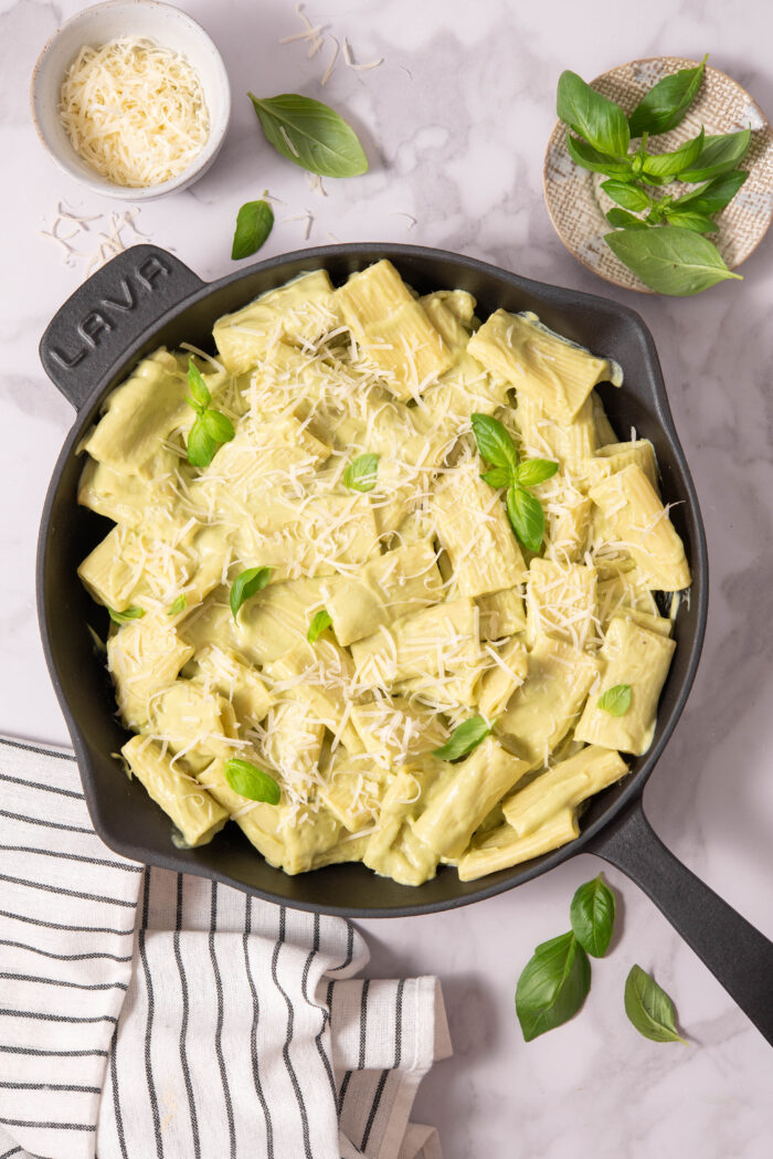 A skillet with avocado pasta, topped with vegan parmesan and basil.