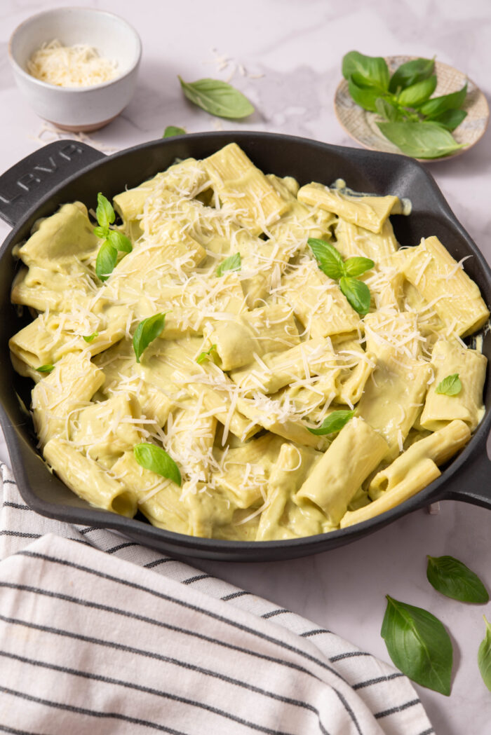 A skillet full of creamy vegan avocado pasta with vegan parmesan and fresh basil.