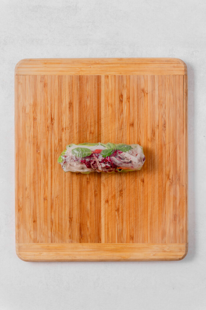 A fully assembled summer roll with rice vermicelli, tofu, and fresh veggies.