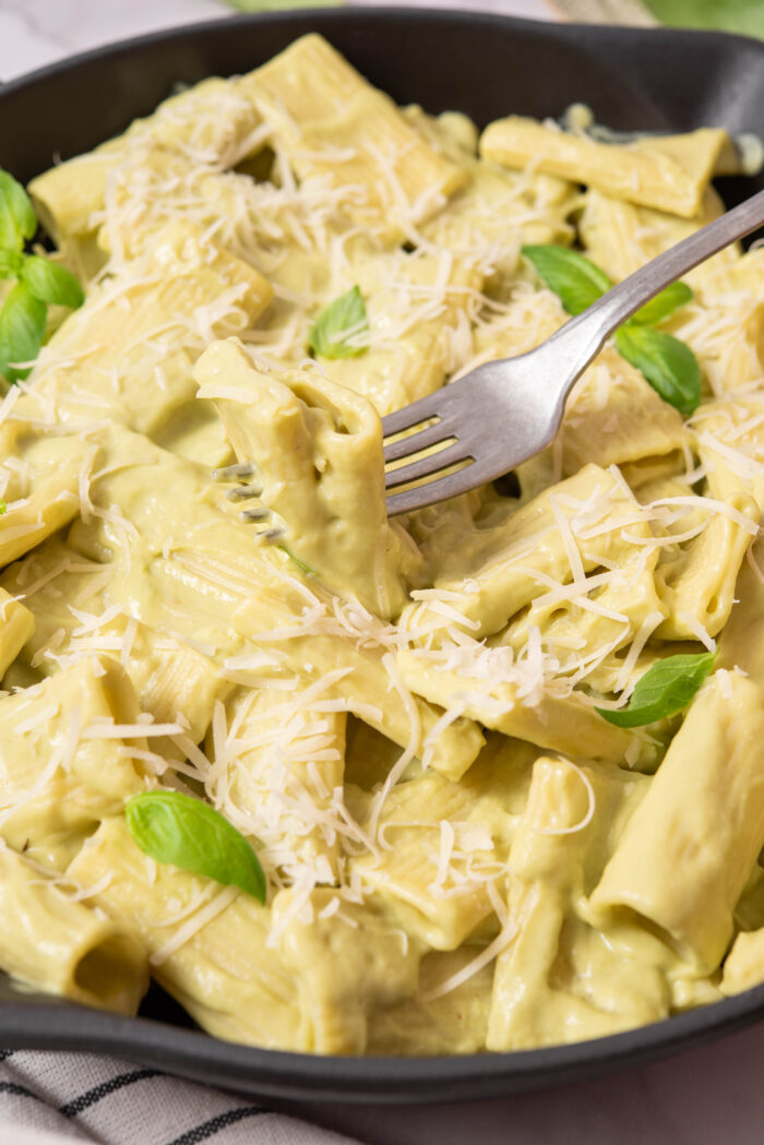 A close up shot of a fork picking up soe avocado pasta.