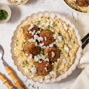 Creamy zuchini orzo bowl, served with vgean meatballs, fresh herbs and vegan feta.