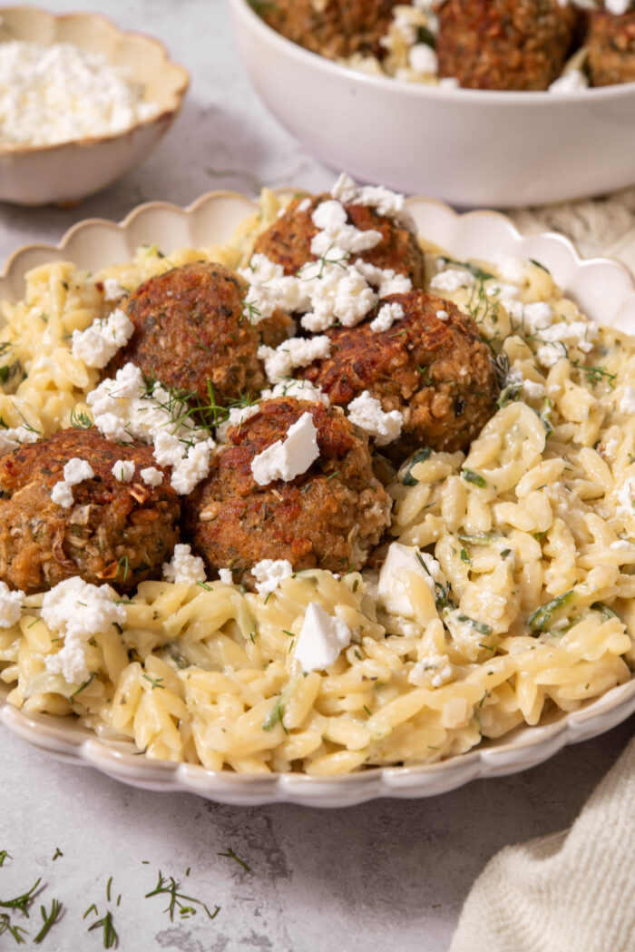 Close up of the creamy zucchini orzo in a bowl, served with vegan feta and vegan meatballs.