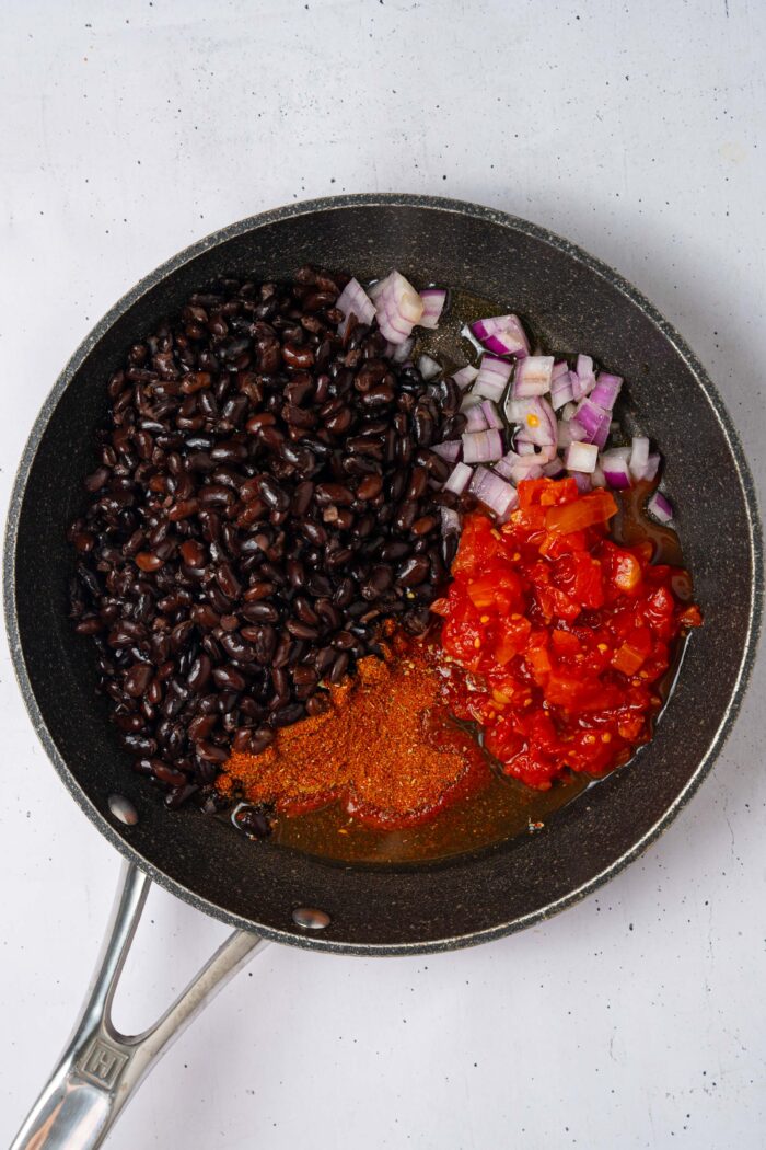 The bean topping ingredients added to a large pan, inlcuing tomatoes, onions, and black beans.