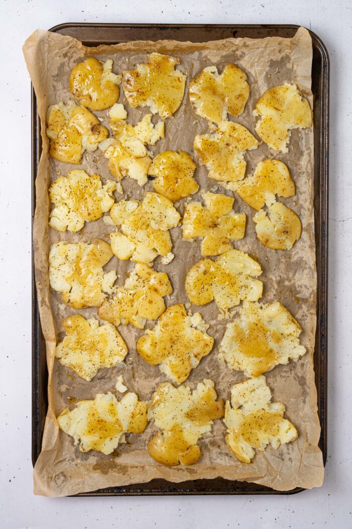 Smashed boiled potatoes spread on a baking tray and sprayed with oil.