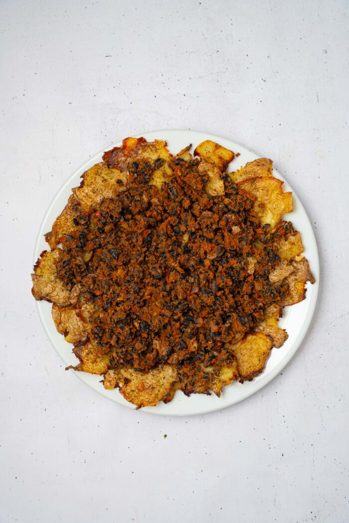 Smashed crispy potato nachos served on a platter and topped with spiced black beans.