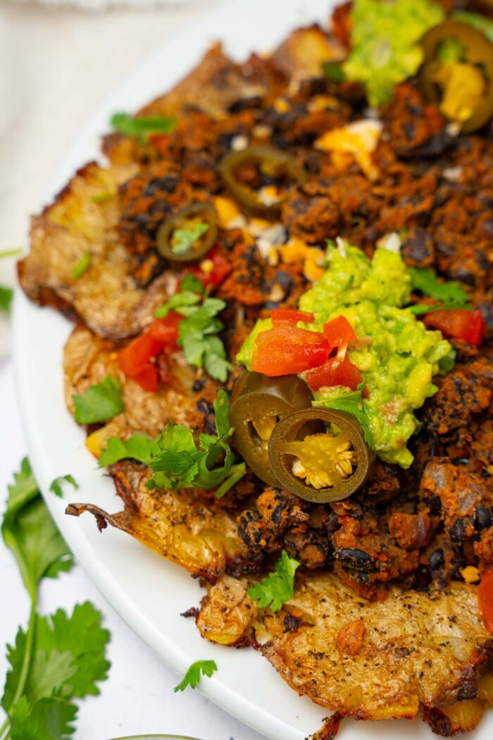 A close up of smashed potato nachos with black beans and other toppings.
