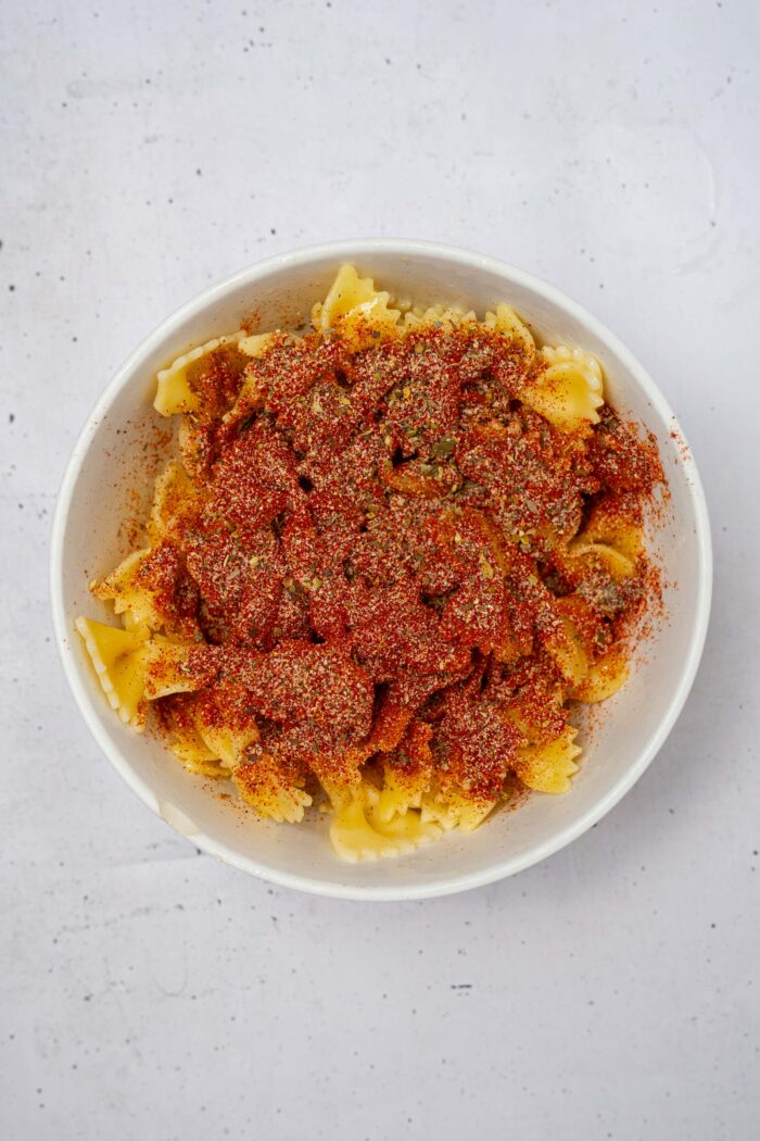 Cooked pasta, topped with spices in a mixing bowl.