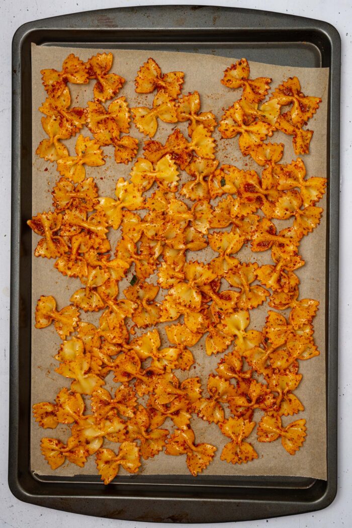 Seasoned bow tie pasta spread on a lined baking sheet.