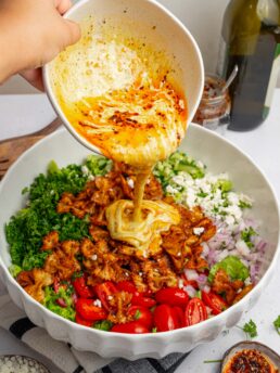 A creamy dressing with a chili swirl being poured over the crispy pasta salad.