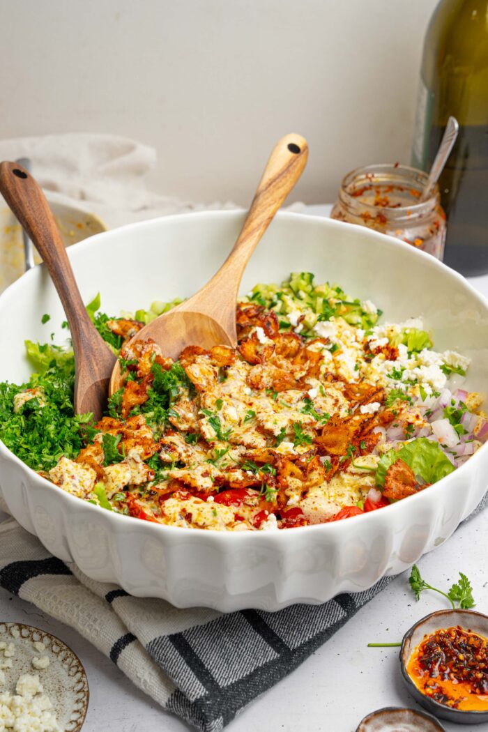 A large bowl of crispy pasta salad with the dressing over the top and two serving spoons.