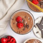 A top down shot showing a cup of blended chocolate chia pudding garnished with raspberries and chocolate.