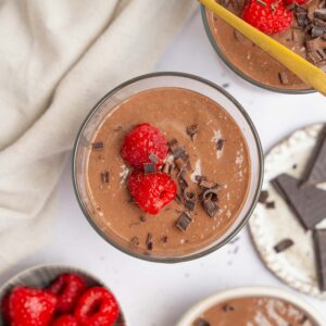 A top down shot showing a cup of blended chocolate chia pudding garnished with raspberries and chocolate.