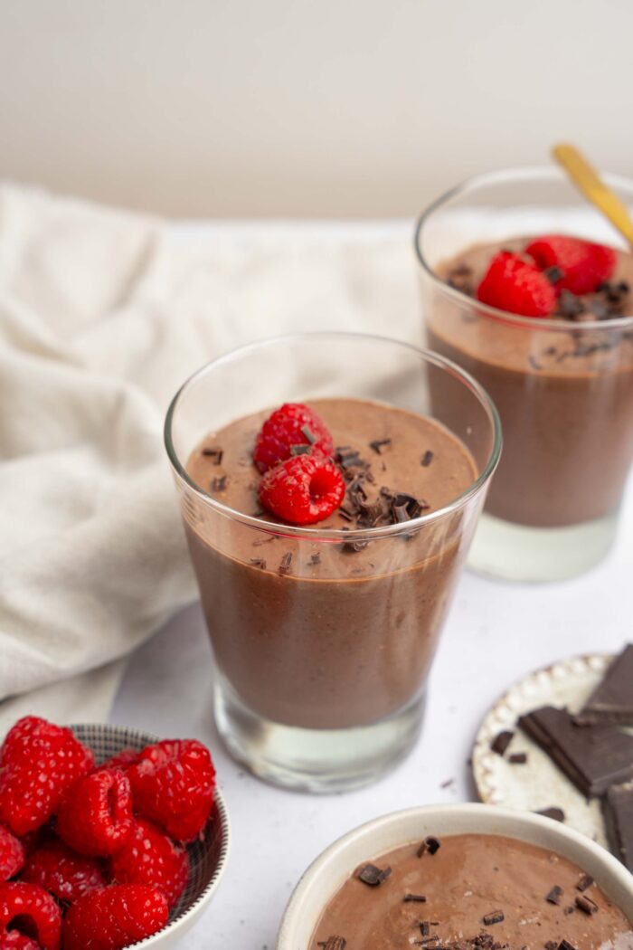 Two cups of blended chocolate chia pudding served with chocolate shavings and raspberries.